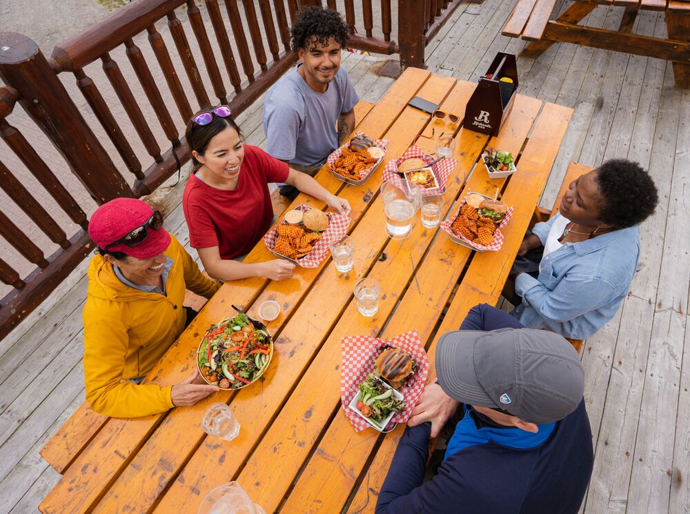 A group of friends enjoys food and drinks on a patio at Sunshine ski resort in Banff National Park. 